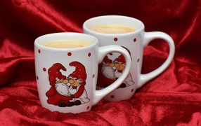 Две белые чашки кофе с рисунком стоят на красной ткани