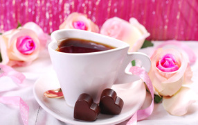 White cup in the shape of a heart with coffee on a saucer with candies