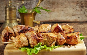 Appetizing kebab lies on a cutting board with lettuce leaves