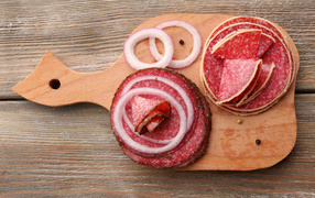 Аппетитные кусочки колбасы на разделочной доске с кольцами лука