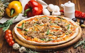 Fresh pizza with meat and cucumbers on the table with vegetables