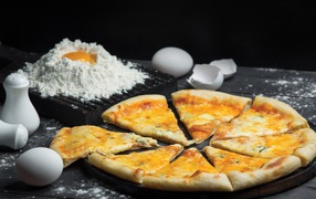 Пицца с сыром нарезана кусочками на столе с мукой и яйцами