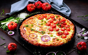 Pizza with tomatoes and onions on a tray with vegetables