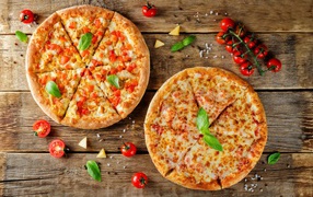 Two pizzas with cheese and bell peppers on a table with tomatoes