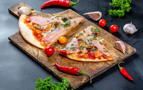 Two slices of pizza on a cutting board with red pepper and garlic