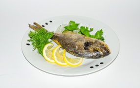 Запеченная рыба на тарелке с лимоном и зеленью 