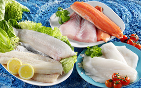 Филе рыбы на тарелках с помидорами и листьями салата