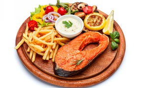 Fish on a board with french fries, vegetables and sauce