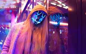 Girl in a hoodie and a neon mask against the wall