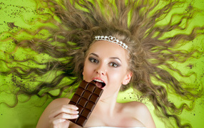 Красивая девушка с украшением в волосах лежит с шоколадкой 