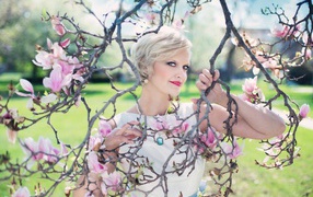 A beautiful short-haired woman stands by a flowering magnolia