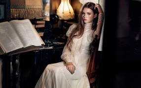 Девушка в красивом белом платье сидит на стуле у стола