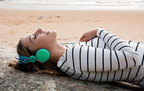 Молодая девушка лежит в наушниках на земле у моря