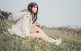Девушка азиатка в пальто сидит на траве