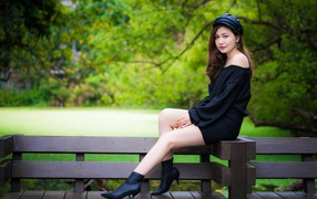 Красивая девушка азиатка в черном платье сидит на деревянной лавке