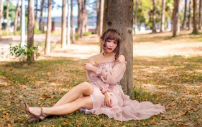 Красивая девушка азиатка в платье сидит под деревом