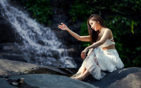 Красивая девушка азиатка в белом платье сидит у воды
