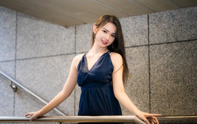 Красивая азиатка в черном платье стоит у перил