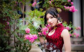 Красивая азиатка с веером в руках стоит у куста с розовыми цветами