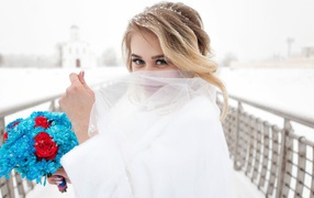 Красивая невеста с букетом в руках закрывает лицо фатой