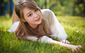 Beautiful brown-eyed Asian girl lying on green grass