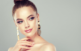 Красивая девушка шатенка с золотыми серьгами в ушах на сером фоне