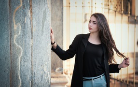 Красивая девушка в черном пиджаке стоит у стены