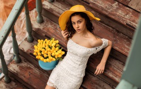 Красивая девушка в белом платье и желтой шляпе на ступеньках с букетом тюльпанов