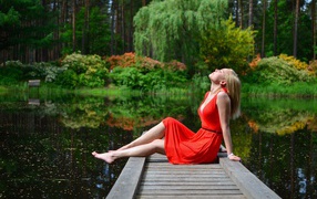 Beautiful girl sitting in a red dress on the bridge