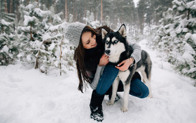 Красивая девушка с собакой породы хаски в заснеженном лесу 