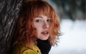 Beautiful red-haired girl stands by a tree in winter