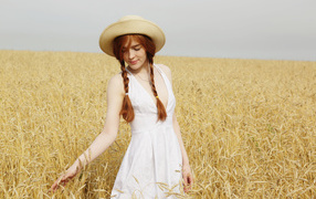 Красивая рыжеволосая девушка гуляет по полю с пшеницей