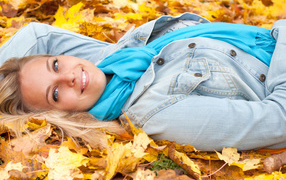 Красивая улыбающаяся девушка лежит на желтых листьях 