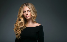 Beautiful young girl with long hair in a black dress on a gray background