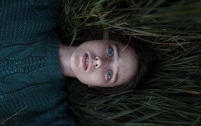 Голубоглазая девушка в свитере лежит на траве