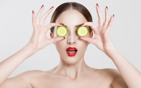 Яркая девушка с огурцами у глаз на сером фоне