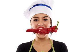 Девушка в шапке повара с красным перцем во рту на белом фоне