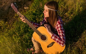 Девушка с гитарой сидит в лучах солнца на траве