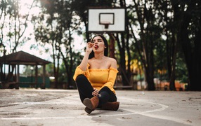 Девушка с леденцом сидит на баскетбольном поле