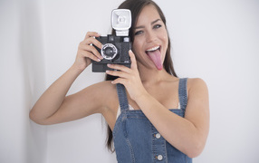 Девушка с высунутым языком с фотоаппаратом в руках