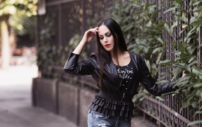 Длинноволосая брюнетка в черной куртке у забора