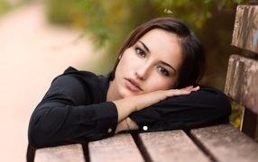 Грустная кареглазая девушка лежит на деревянной лавке