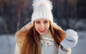 Улыбающаяся девушка в теплой шапке и варежках зимой
