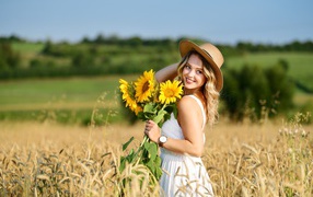 Smiling girl on the field with wheat with a bouquet of sunflowers in hand