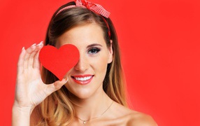 Улыбающаяся девушка с бумажным сердцем у лица на красном фоне