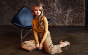 Девушка сидит на полу около черного кресла 