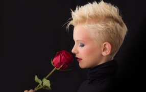 Девушка блондинка с короткой стрижкой с розой в руках на черном фоне