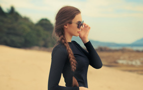 Девушка с косой в черных очках смотрит на воду