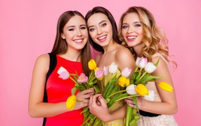 Три красивые девушки с букетами тюльпанов на розовом фоне