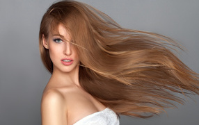 Ветер развивает волосы красивой девушки на сером фоне